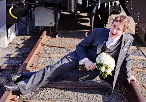 groom holding a bouqet laying on train tracks