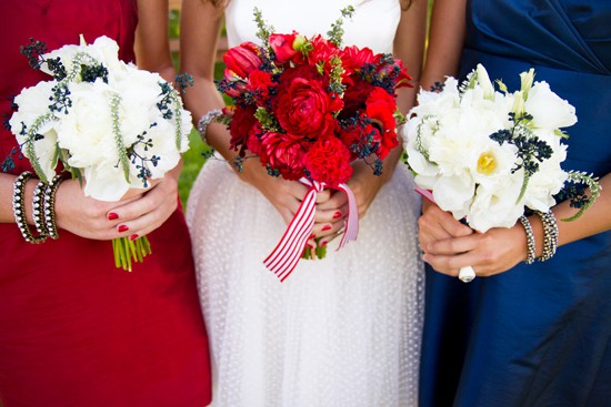 woman in a red dress holding white floral bouquet, woman in white holding a red bouquet wrapped with a red and white ribbon and woman in blue holding a white flower arrangement