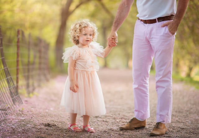 small girl with light pink dress holding mans hand in the park