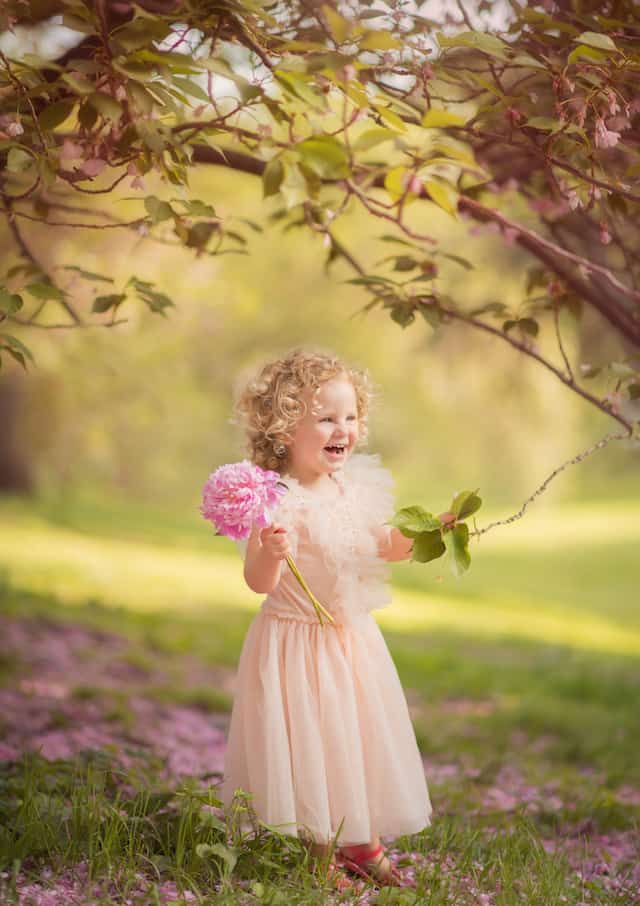 young girl smiling wearing a light pink dress holding long stem pink flower
