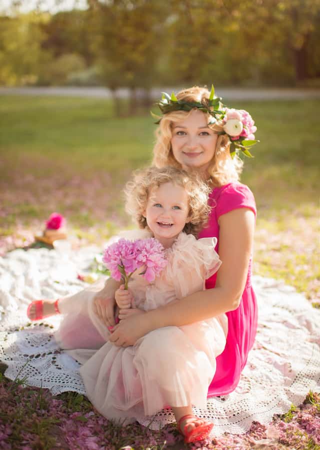 Mom and daughter siting on white blanket wearing pink dresses