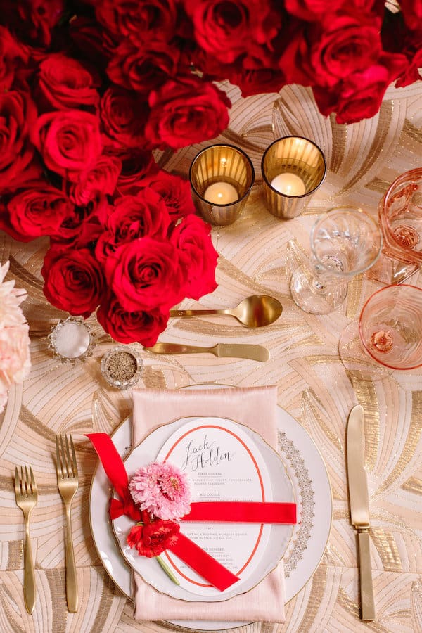 Overhead of placesetting with gold silverware and red roses and lit candles