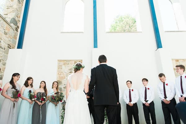 springtime blooms by the box bride and groom getting married with backs to the camera and front view of wedding party looking at them