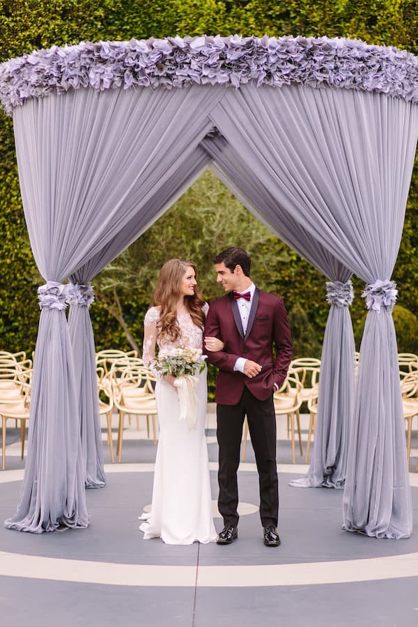 Hollywood Wedding, Glamorous, Bloomsbythebox bride and groom under a decorated purple outdoor tent groom wearing burgundy blazer