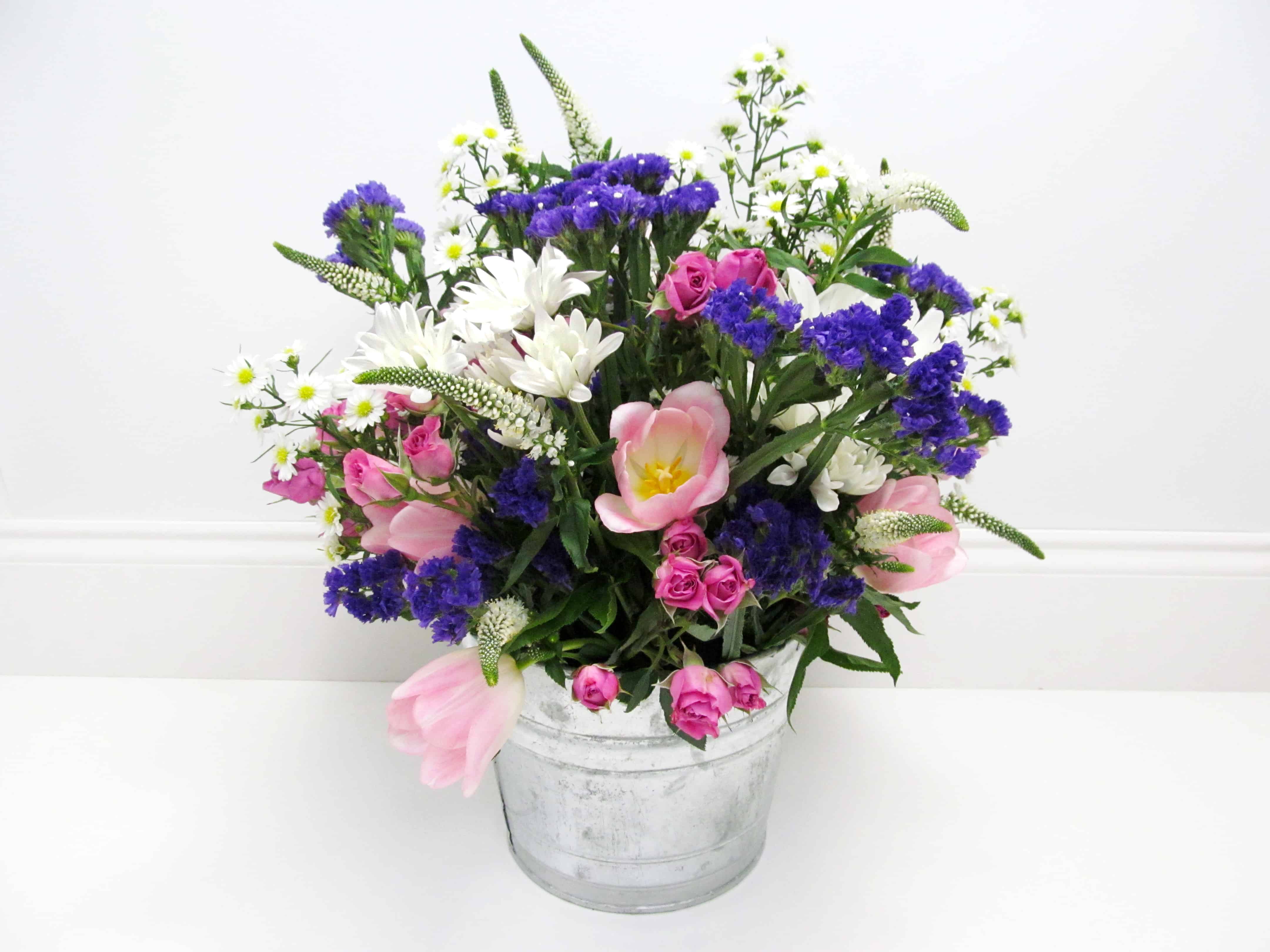 DIY English Cottage centerpiece with Pink Tulips, Pompon Daisies, Purple statice, pink spray roses, and monte casino aster in a silver metal bucket