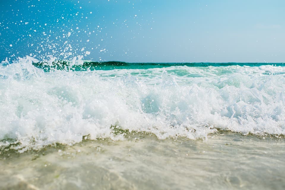 close up of a breaking wave with white foam on blue water and sand