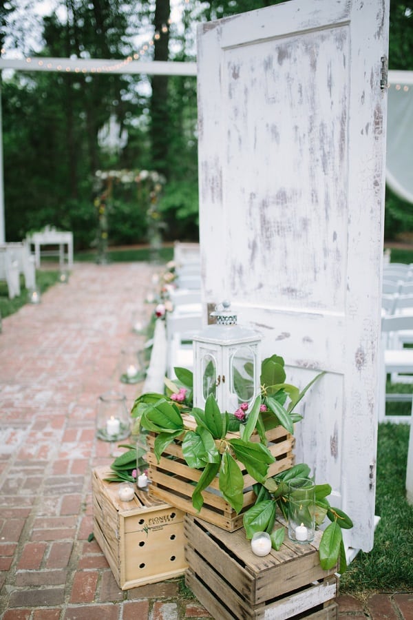 Decorative setting with white lantern at begging of wedding aisle outdoors with arch in background