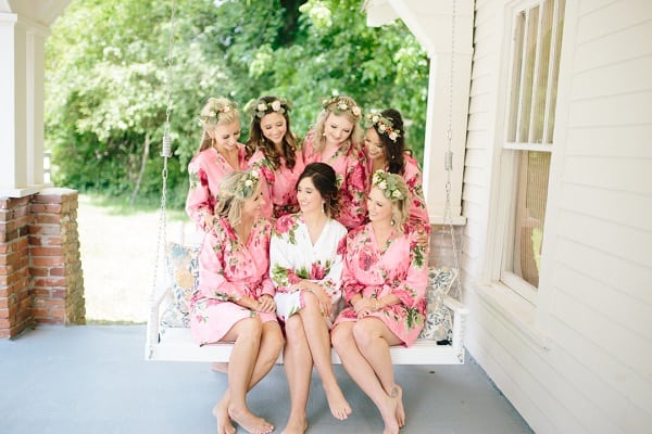 Bride and 6 bridesmaids in pink robes on front porch swing