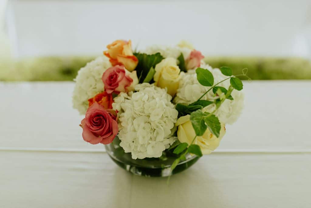 pink, orange, and yellow roses, with white hydrangeas centerpiece in a glass vase