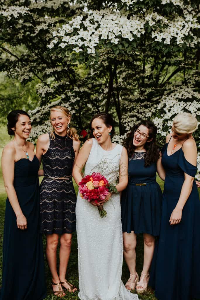 bride holding red orange and yellow bridal bouquet laughing with four friends outside
