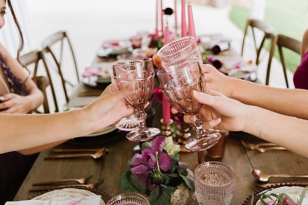 extended arms and hands touching glasses with wooden table background