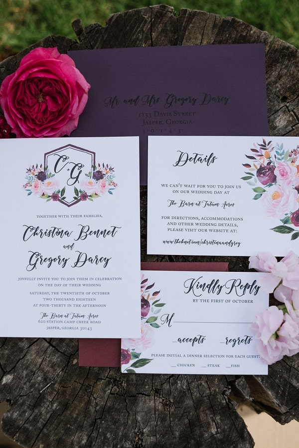 Various parts of a wedding invitation laid out with one red flower