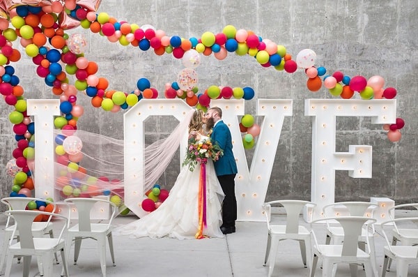 bride and groom kissing in front of love sign with colorful balloons