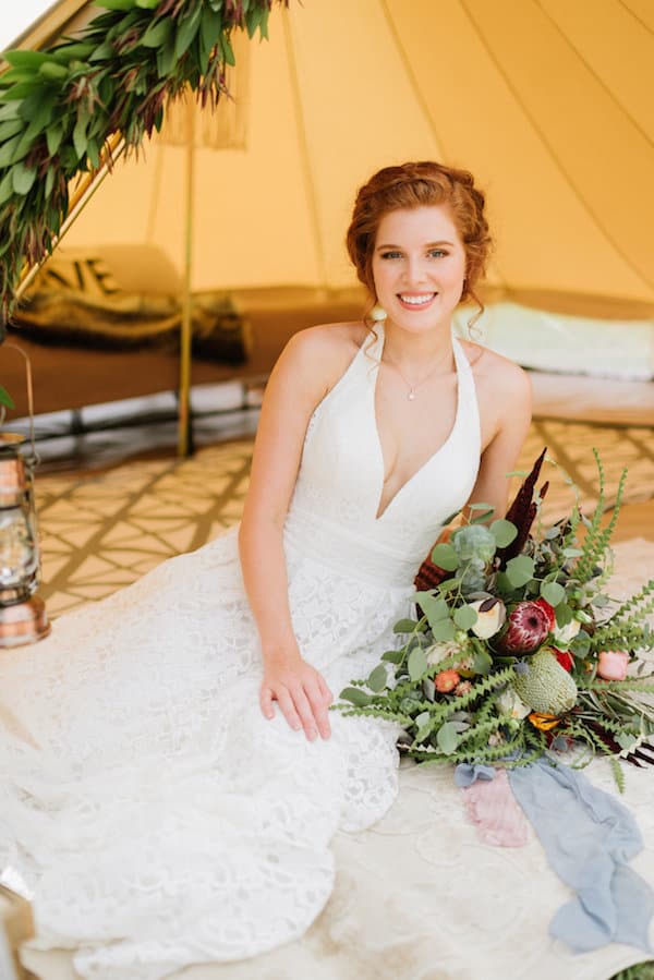 Bride relaxing in tent with large floral bouquet
