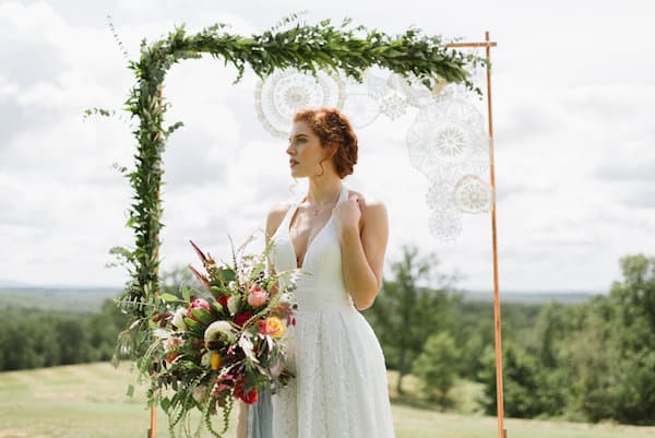 Bride with large floral bouquet in front of arch with garland