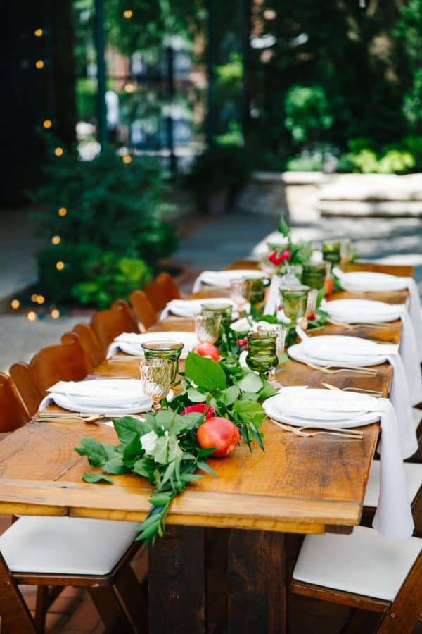 long wooden table with placesettings long green garland table runner and peaches