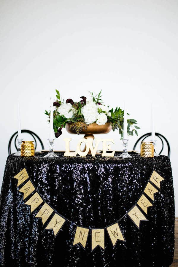 table with black table cloth and sign saying happy new year with white flowers