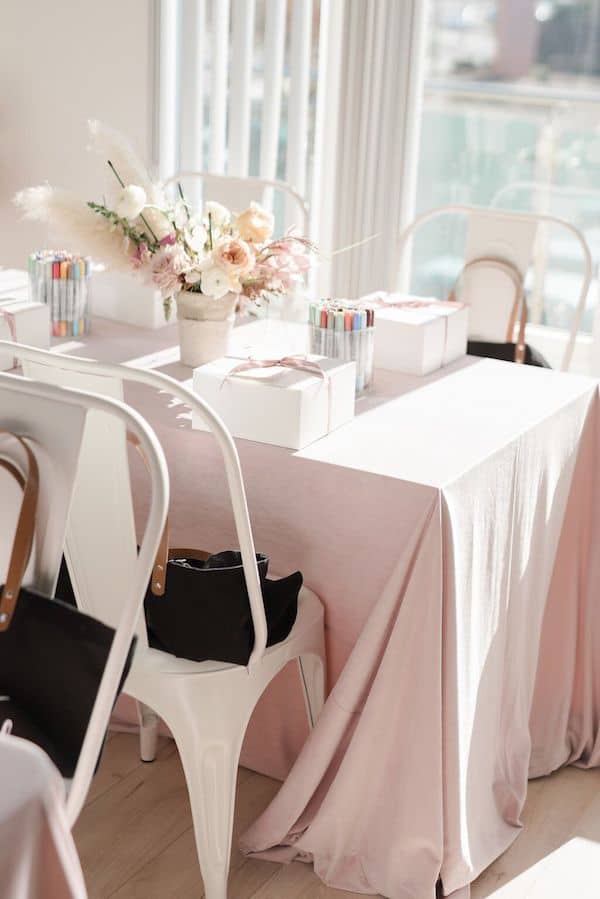 long tables with pink tablecloths and art supplies, a box with a bow on it and flowers