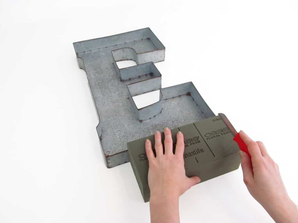 sheet metal cutout of the letter E with hands cutting floral foam