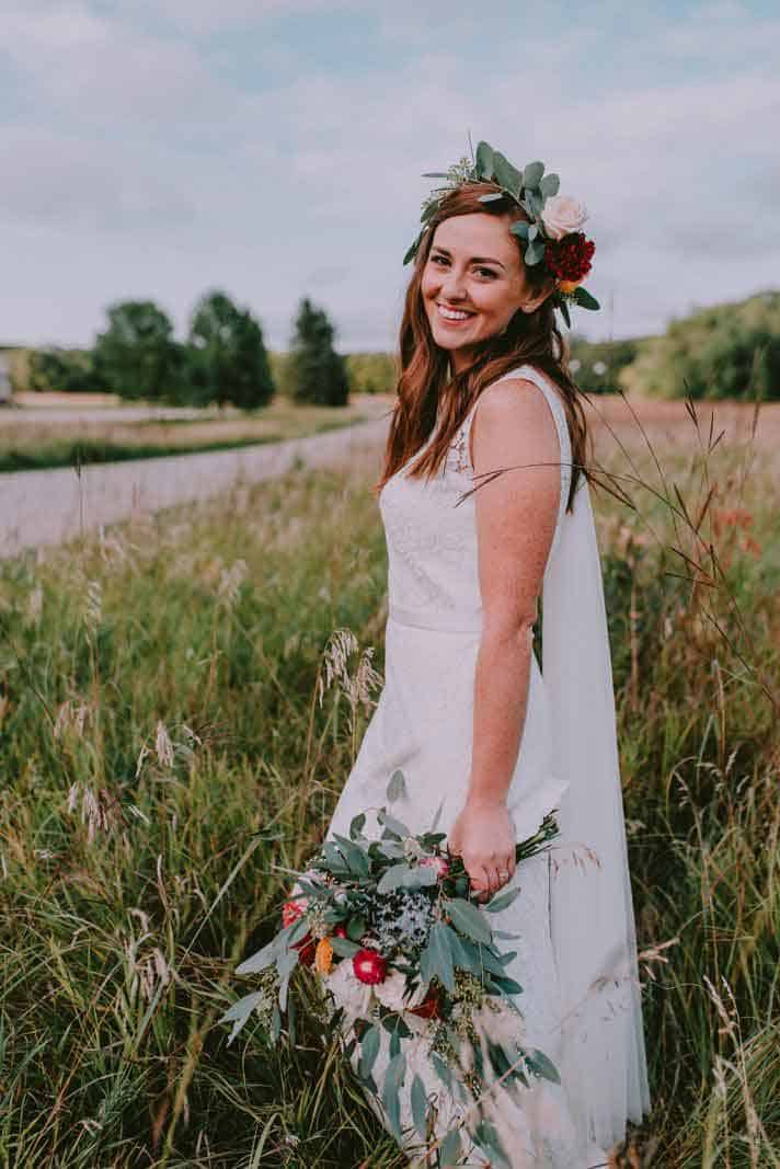 bride with floral crown and bouquet standing near a road in a field