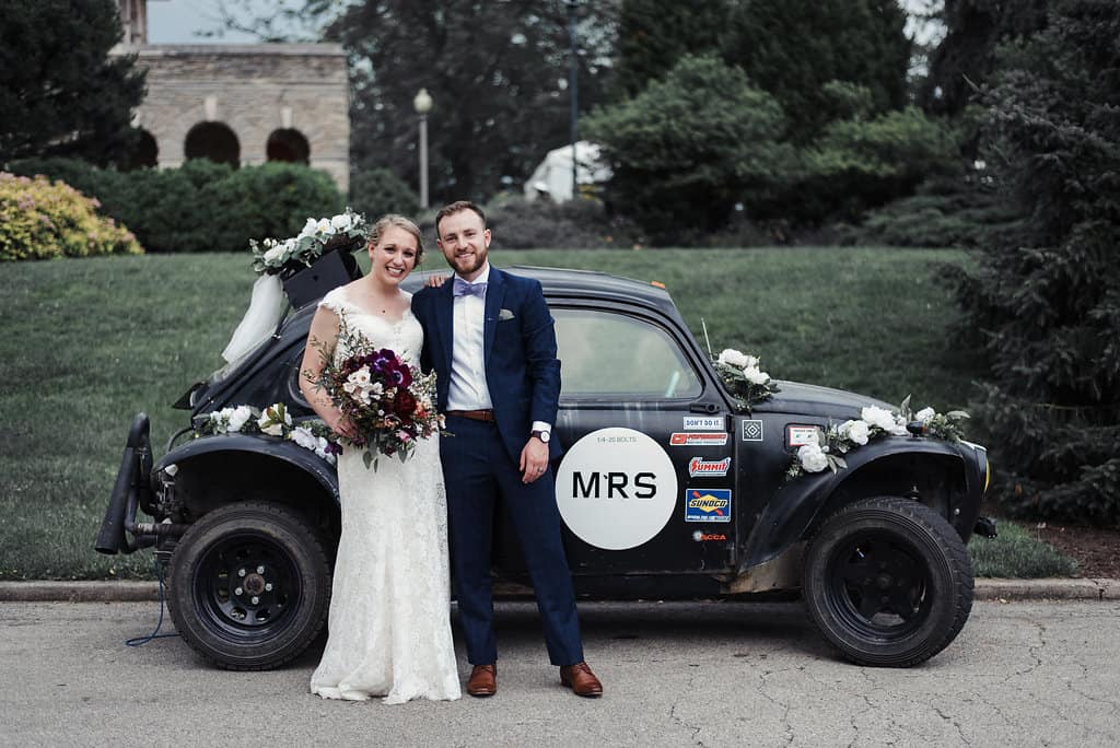 Bride and groom standing in front of black car