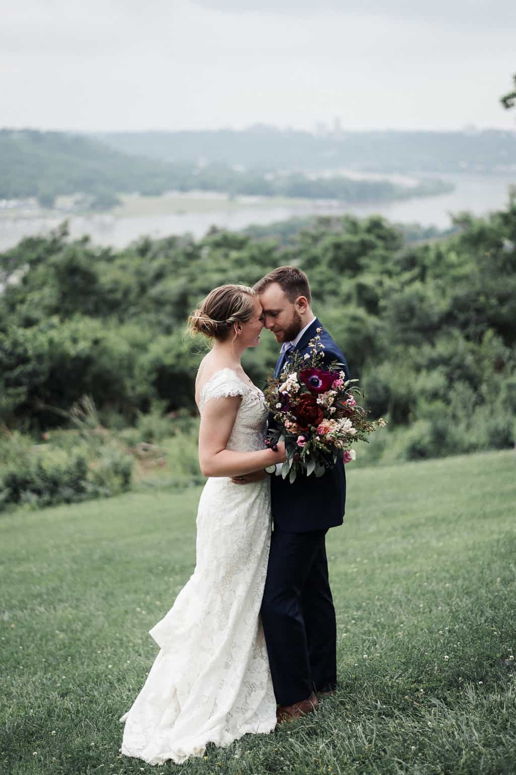 bride and groom standing on a hillside embracing