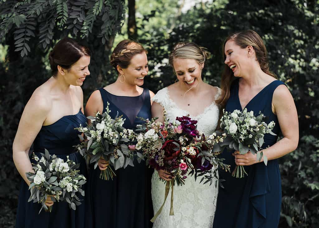 bride holding moody deep red and purple bouquet with bridesmaids in blue dresses with bouquets