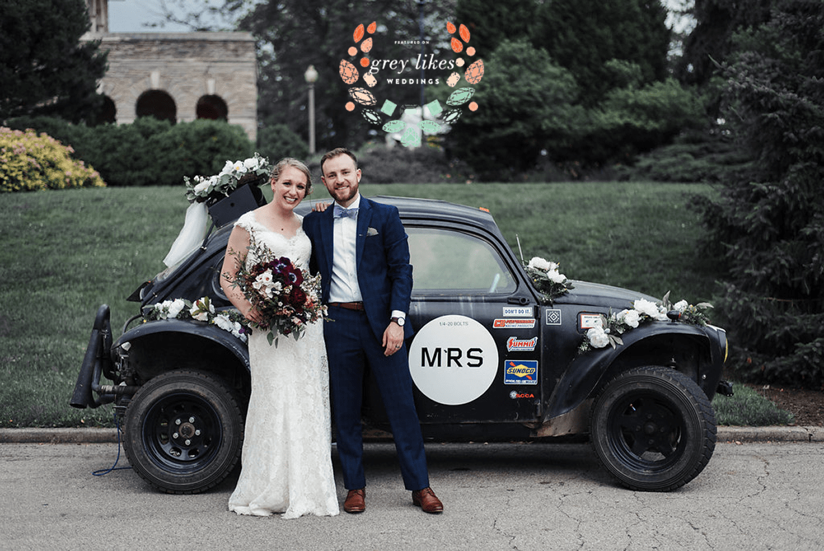 bride and groom in front of black car decorated with flowers