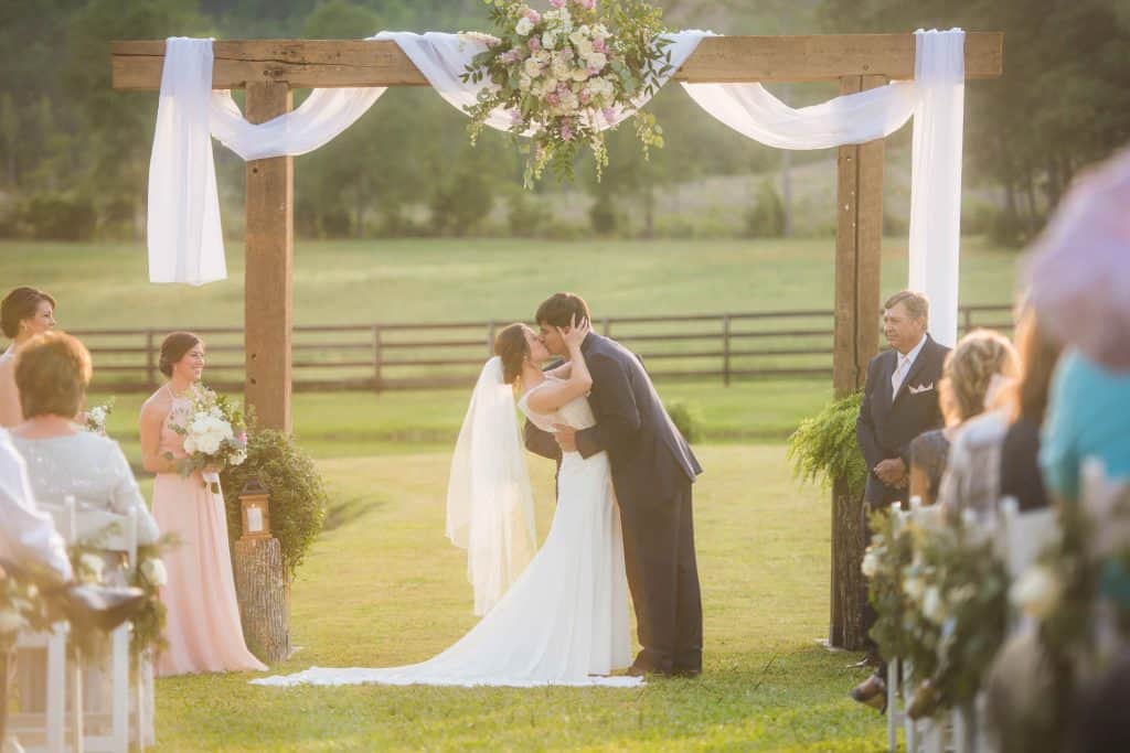 bride and groom kissing under outdoor wooden arbor