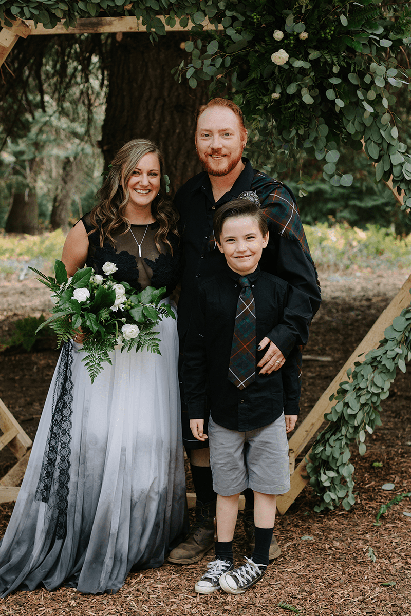 green forest wedding couple under arbor with greens and a small boy