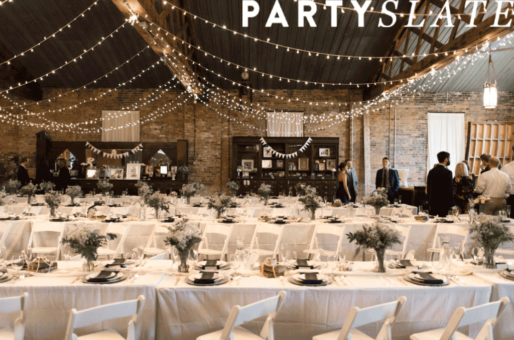 indoor wedding venue with rows of tables and place settings and string lights hung from the ceiling