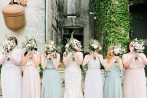 Bride and bridesmaids in pastel dresses with bouquets over thier faces