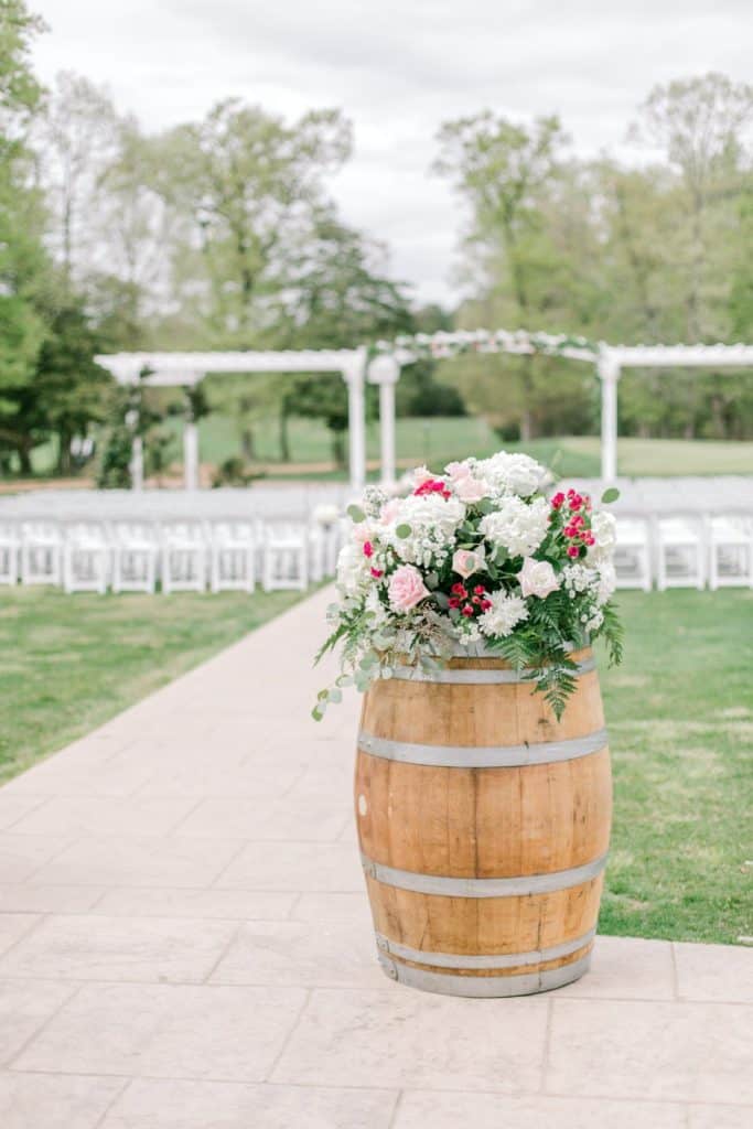 large red and white floral arrangement on wooden barrel with outdoor wedding background