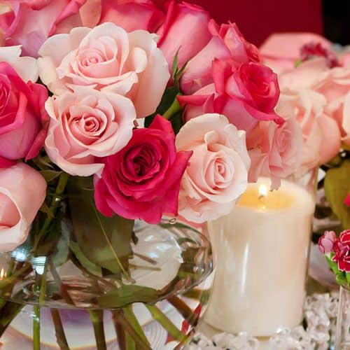pink and peach flower centerpiece vase with water next to a candle