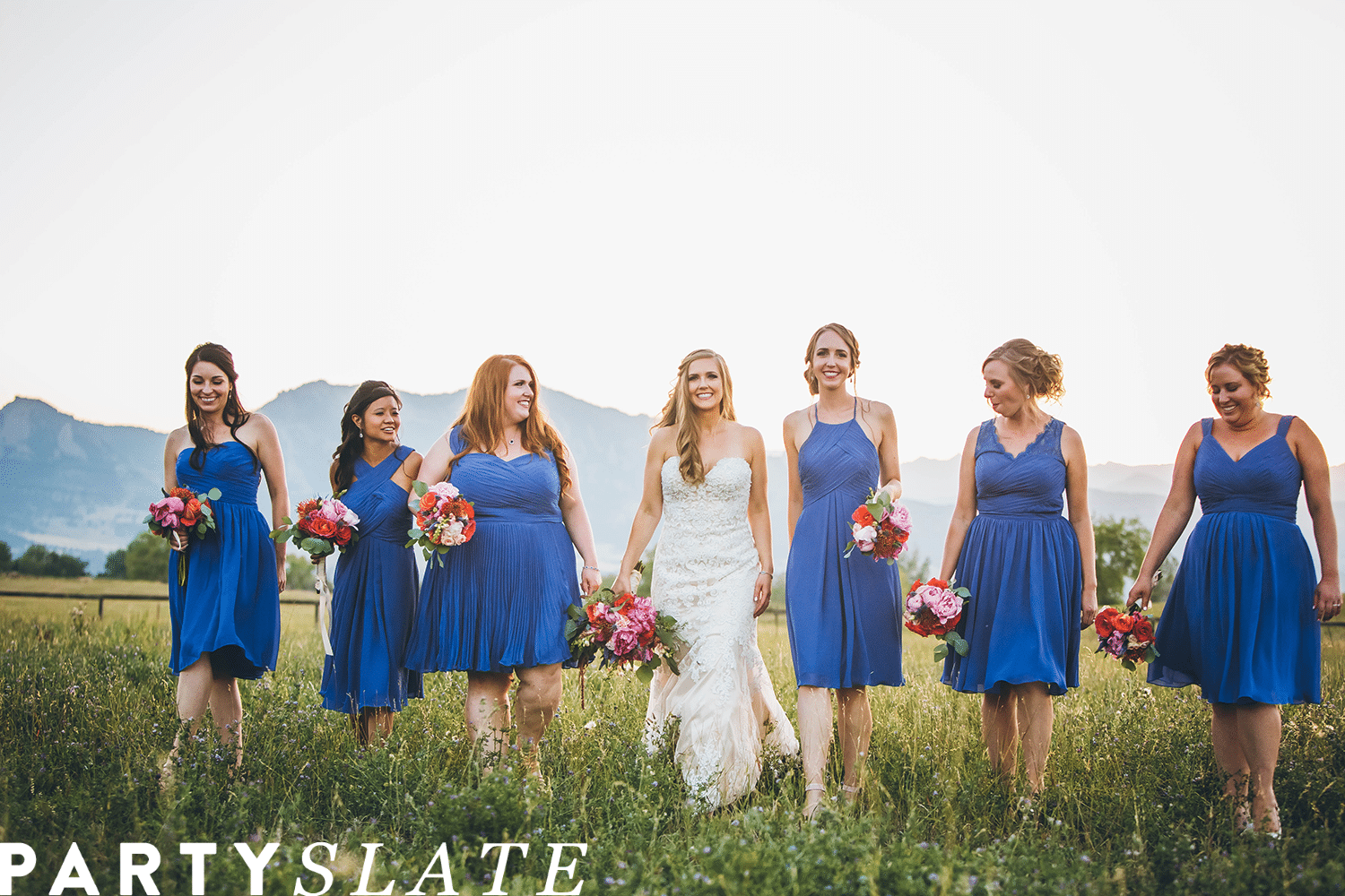 Bride and bridesmaids in blue dresses walking through a field holding flowers