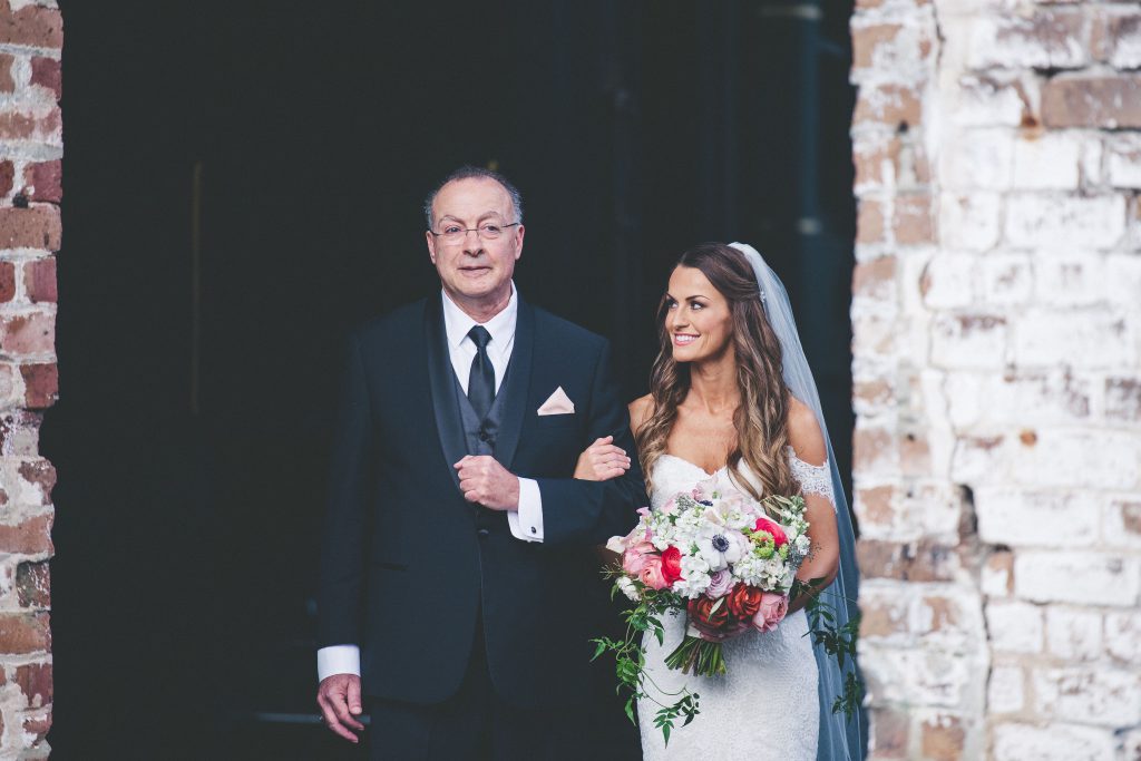 Bride being walked down the aisle holding flower bouquet