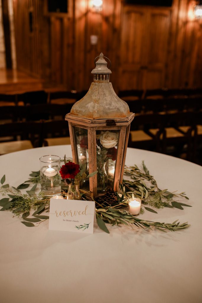 Centerpiece on a table with candles, a lantern with flowers inside and a green stems for decoration