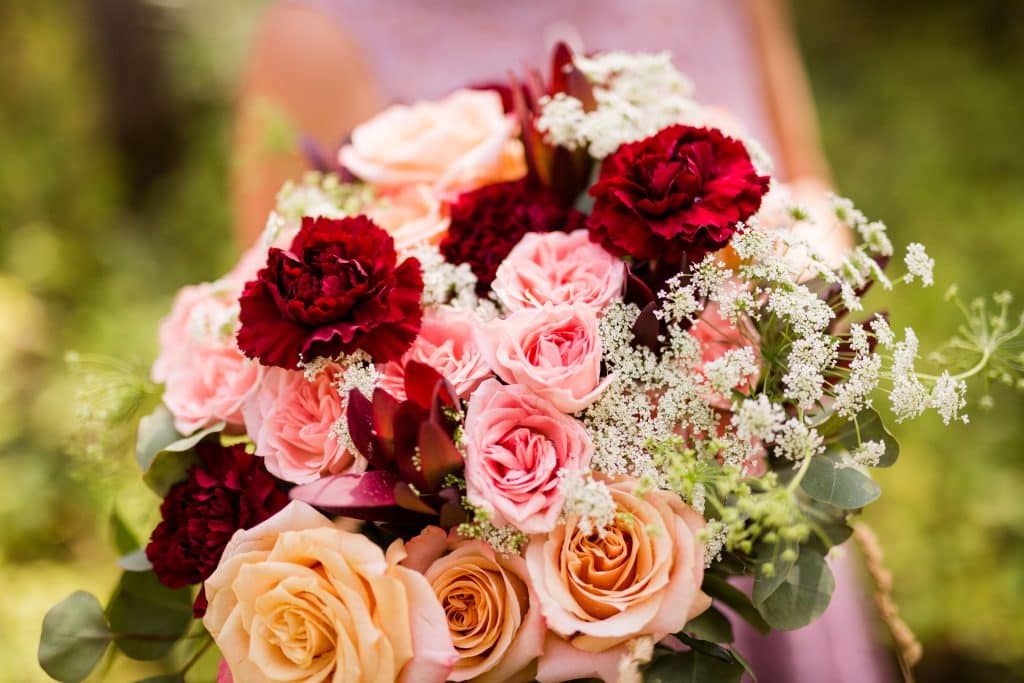 burgundy carnations, pink roses, peach roses, seeded eucalyptus, and Queen Anne’s lace bouquet