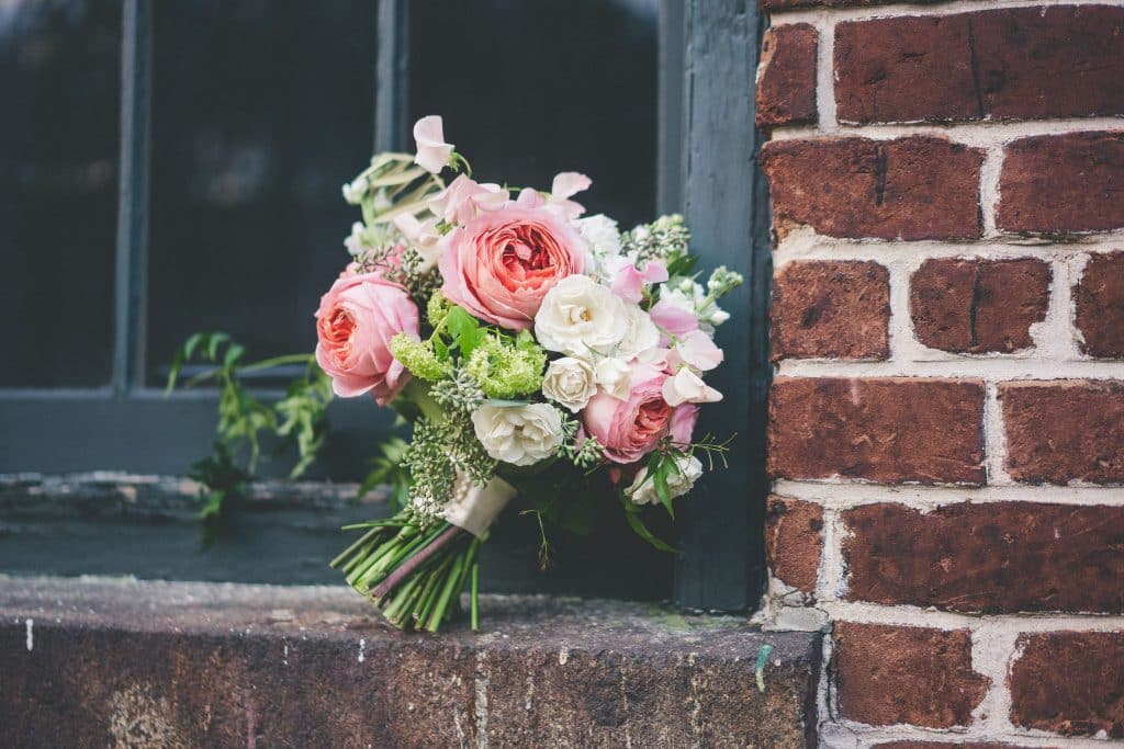 Pink and white garden roses, roses, seeded eucalyptus, sweet peas, and Queen Anne lace bouquet in a brick windowsill