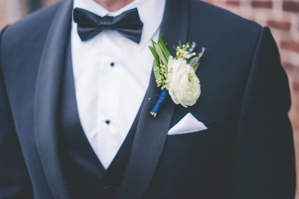 white and green boutonniere comprised of a white ranunculus and seeded eucalyptus greenery