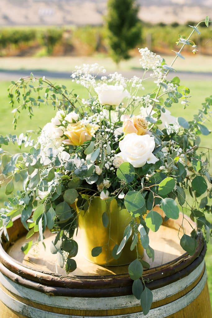 rustic wooden barrel with roses, queen Anne’s lace, silver dollar eucalyptus, and baby blue eucalyptus in metallic gold vase