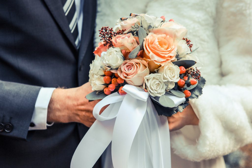 Two people holding a bouquet with pink flowers