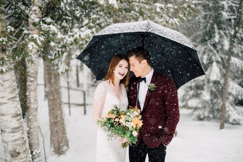 Couple in the woods with umbrella protecting them from snow