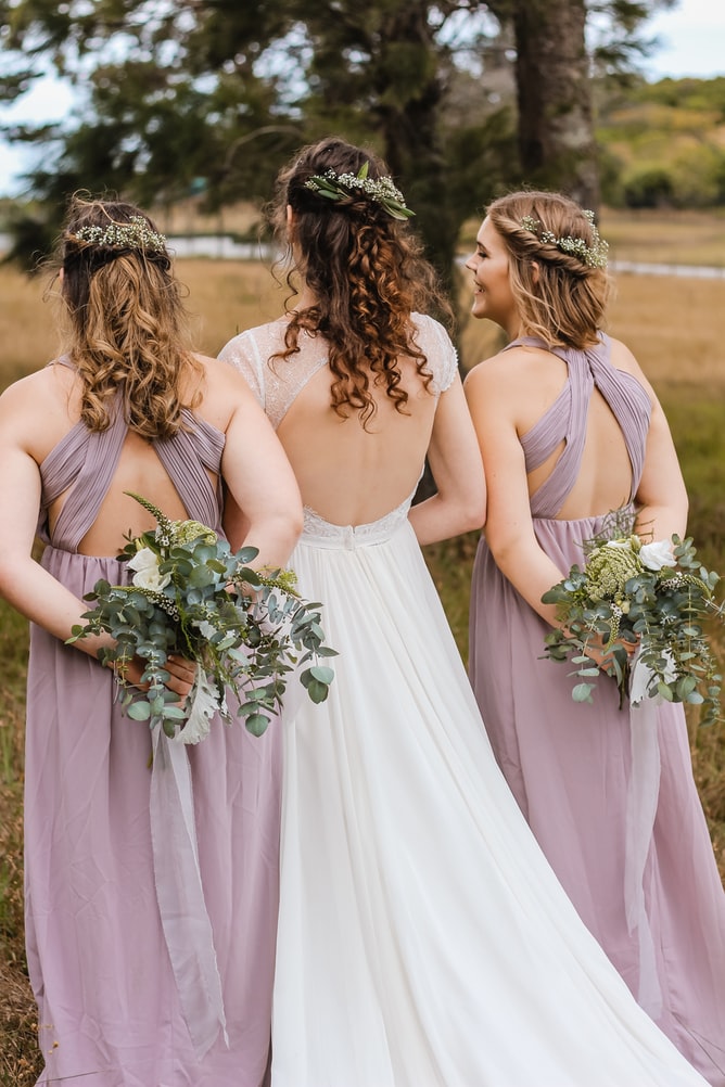bride and bridesmaids facing away holding bouquets of flowers behind their backs