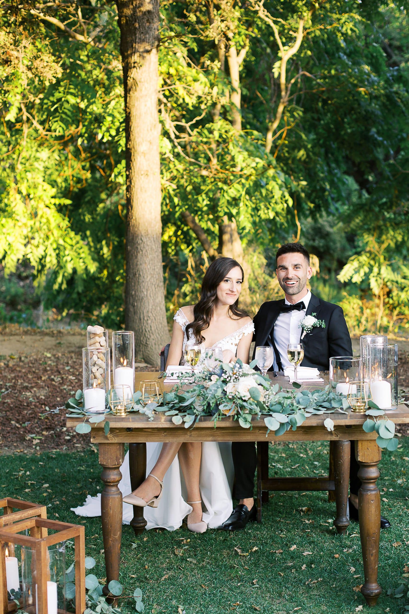 Outdoor wedding with bridge and groom at a table with candles and green flower decoration