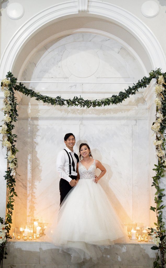 All white wedding bride and groom in archway with candles