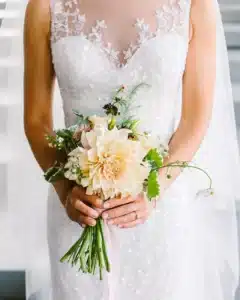 A bride holding a petite bouquet of flowers in peach and burgundy.