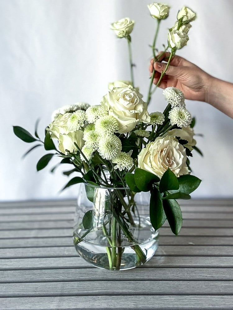 white flowers and roses being placed in a glass vase with water