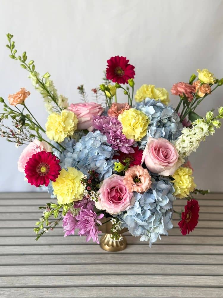 a compote flower arrangement with pastel and hot pink flowers.