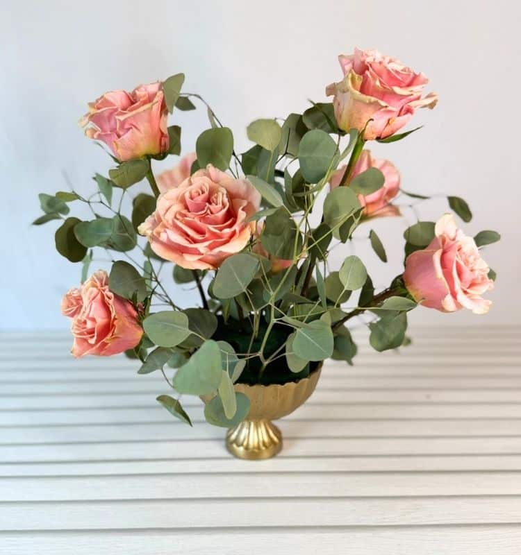 a centerpiece being made with eucalyptus and peach roses